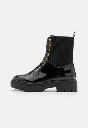Bottines en cuir verni noir avec une tige en tissu texturé à nervures, œillets dorés, lacets noirs et semelle robuste.
