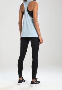 Canottiera senza maniche blu chiaro con schiena scoperta e tessuto testurizzato, abbinata a leggings neri e scarpe da ginnastica nere con dettagli bianchi.