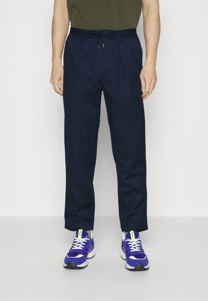 Mörkblå, löst sittande byxor med elastiskt midjeband och dragsko. Bärs med lila träningsskor som har gröna detaljer och vita snören.