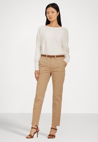 Off-white dlouhý rukáv, khaki tapered kalhoty s bočními kapsami, hnědý opasek a hnědé sandály na vysokém podpatku. Jednoduchý, přiléhavý design.