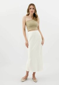 Olivově zelený pruhovaný crop top s řemínkem, v kombinaci s volnou bílou saténovou midi sukni a zlatými nazouvacími botami. Hladký, minimalistický design.