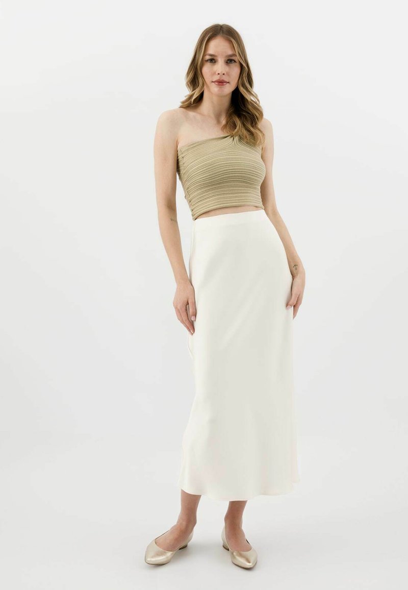 Olivově zelený pruhovaný crop top s řemínkem, v kombinaci s volnou bílou saténovou midi sukni a zlatými nazouvacími botami. Hladký, minimalistický design.