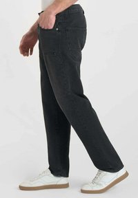 Pantalons en velours côtelé noirs à coupe droite, avec des poches avant et une fermeture à bouton, assortis à des baskets blanches.