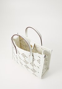 Hvit skinn tote bag med utskåret geometrisk mønster, kontrasterende brune håndtak og en strukturert form for ekstra stabilitet.
