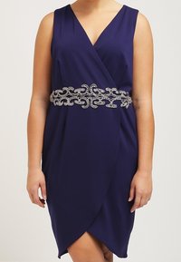 Námořnická modrá zavinovací šaty s hlubokým V výstřihem, s dekorativním korálkovým pásem a měkkou, splývavou tkaninou. Elegantní drapérie vytváří lichotivou siluetu.