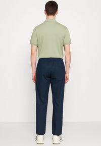 Polo shirt verde chiaro con maniche corte, abbinato a pantaloni blu navy aderenti, con una vestibilità ampia, dotati di una vita elastica e una tasca posteriore.