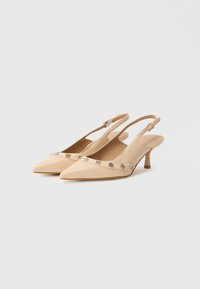 Zapatos slingback beige con punta puntiaguda y tacón bajo. Presentan detalles decorativos de metal a lo largo de la correa y un material sintético liso.