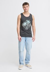 Graues Baumwolltanktop mit einem Palmenbaum-Design und Text. Kombiniert mit hellblauen Jeans und beigen Sneakers. Einfaches Design, lässiger Schnitt.