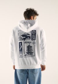 White hoodie featuring a blue graphic print of Mount Fuji, a pagoda, and Japan's outline on the back. Cotton material, relaxed fit.