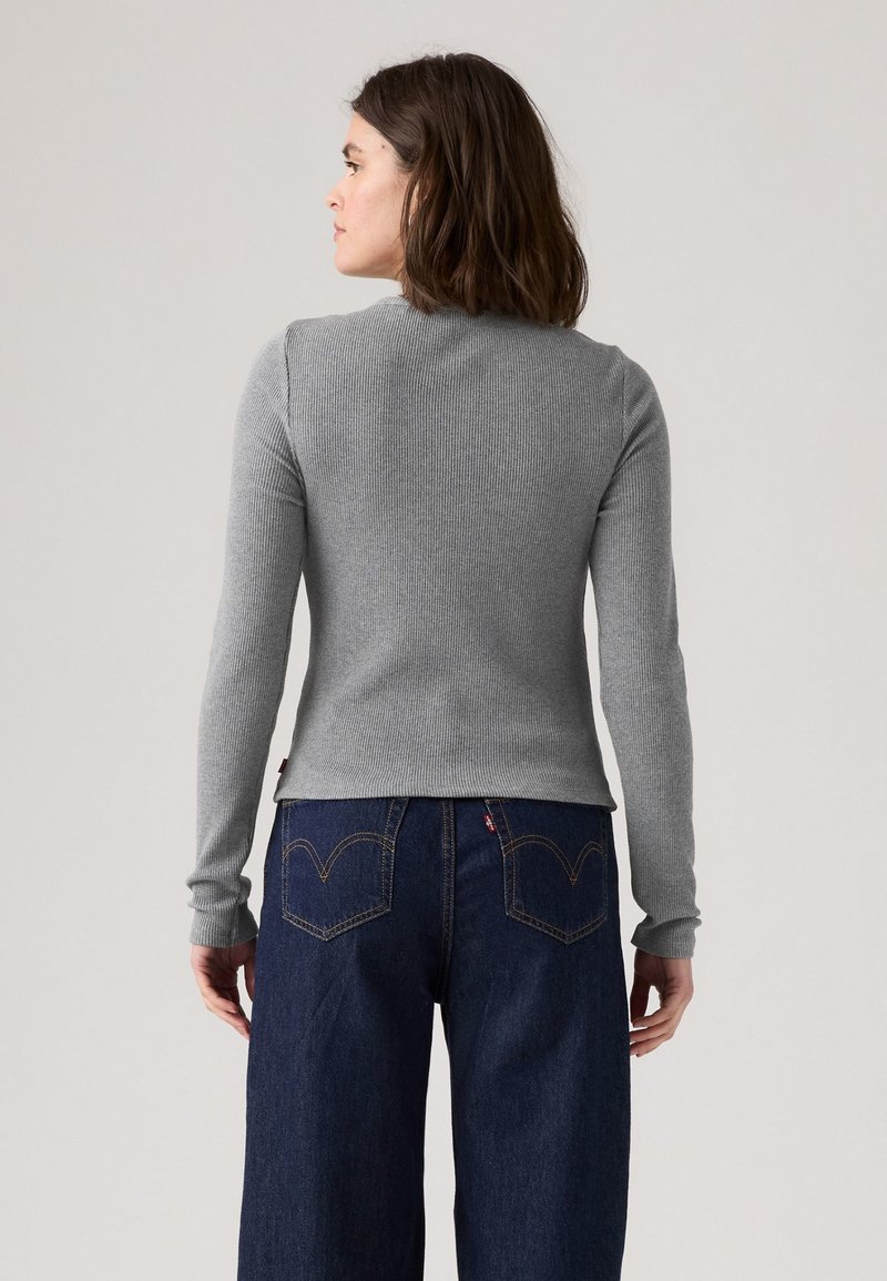 Graues, geripptes Langarmshirt mit taillierter Silhouette und rundem Ausschnitt, kombiniert mit dunkelblauen, weit geschnittenen Jeans, die kontrastierende Nähte aufweisen.