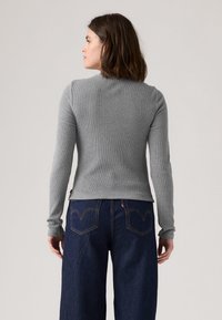 Maglia a maniche lunghe grigia a coste con silhouette aderente, scollo tondo e polsini slim, abbinata a jeans a gamba larga blu scuro con cuciture sulle tasche.