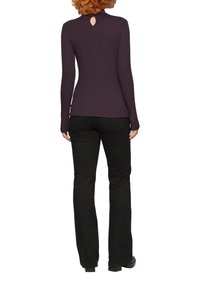 Langärmliges, dunkelviolettes Oberteil mit einem Schlüsselloch-Detail am Ausschnitt, kombiniert mit schwarzen Hosen, die eine figurbetonte Passform und glatte Textur aufweisen.
