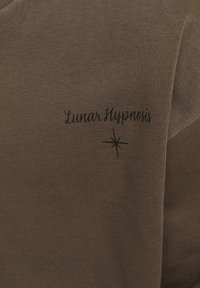 Tela de algodón marrón con una textura suave, que presenta el texto "Hipnosis Lunar" y un pequeño gráfico de estrella en negro.