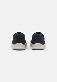 Granatowe buty casualowe z gładkim materiałem wierzchnim, beżową gumową podeszwą, okrągłym noskiem i minimalistycznym designem. Brak widocznego logo lub wzorów.