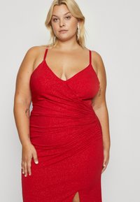 Red, sleeveless dress with a V-neck, ruched texture, and shimmer detail. Features a thigh-high slit, highlighting its fitted silhouette.