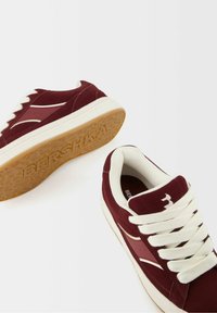 Baskets en daim bordeaux avec lacets blancs et semelle en caoutchouc. Présentent un logo et des accents latéraux subtils. Semelle extérieure texturée pour une meilleure adhérence.