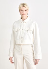 White cropped denim jacket with button closure, two chest pockets, and long sleeves. Features a classic collar and a soft texture.