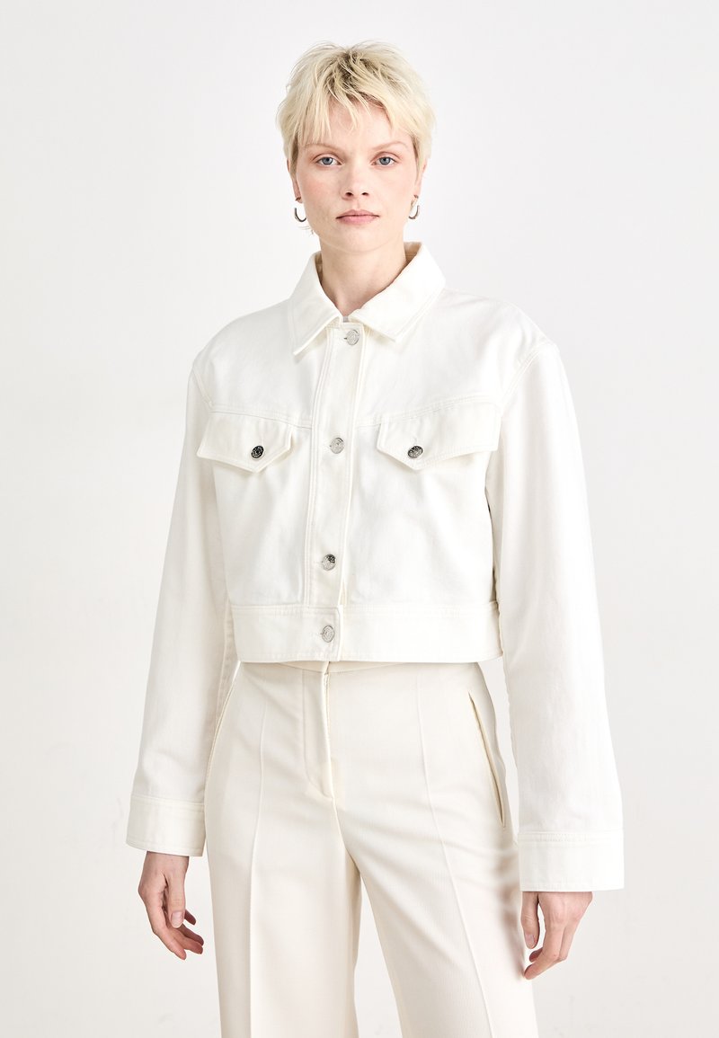 White cropped denim jacket with button closure, two chest pockets, and long sleeves. Features a classic collar and a soft texture.