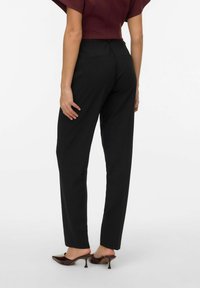 Pantaloni neri su misura con vestibilità slim, una texture liscia e un discreto dettaglio della tasca posteriore. Abbinati a tacchi a punta marroni.