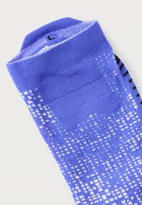 Κάλτσα με μπλε και λευκό σχέδιο, με υφασμένα αντιολισθητικά σημεία στο κάτω μέρος και μαύρες ρίγες κοντά στη φτέρνα, απεικονιζόμενη διπλωμένη σε επίπεδη θέση πάνω σε λευκό φόντο.