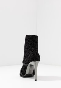 Bottines à talons hauts en imprimé léopard noir avec un design épuré à la cheville et un talon accentué de argent. Texture lisse, découpe ouverte à la cheville avec des sangles légèrement courbées.