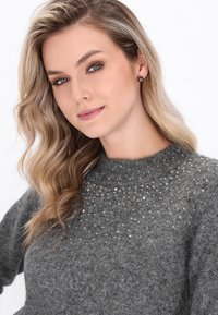 Pulover gri cu un guler înalt și un finisaj texturat, având un model de mici embellishments strălucitoare pe umeri.