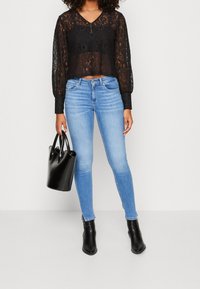 Černý krajkový top na krátké rukávy s dlouhými, nafouknutými rukávy, zkombinovaný se světle modrými úzkými džíny. Drží černou kabelku. Černé kotníkové boty.