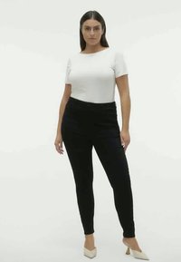 Must musta püksid, mis on kõrge vöökoht, on kombineeritud liibuva valge lühikeste varukatega pluusiga. Mudel kannab beeže kontsakingi ja seisab ühetoonilise valge taustaga.