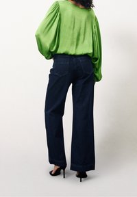 Blouse en satin vert à manches bouffantes et col large, associée à un jean en denim foncé taille haute, avec des poches arrière et une coupe droite.