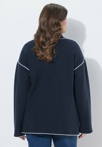 Felpa oversize blu navy con dettagli di cuciture bianche lungo le spalle e l'orlo. Caratterizzata da maniche lunghe e una vestibilità comoda.