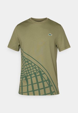 Olíva zöld póló sima anyagból, zöld geometrikus mintával az egyik oldalán és egy kis Lacoste logóval a mellkasán.