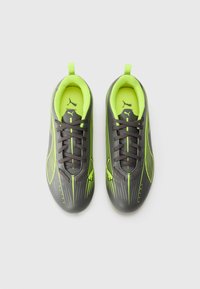 Melnas un neonzaļas futbola kurpes ar elegantu dizainu, teksturētu virsmu un izliekumu; tām ir šņores un aizmugurējais cilpiņš.