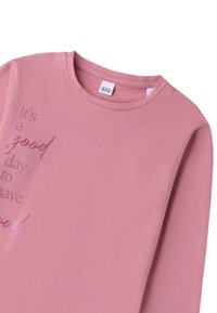 Roze langeliger overhemd van zachte materialen met een geprinte zin in een donkerdere roze gradient. Ronde halslijn en label zichtbaar op de kraag.