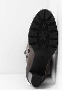 Botte en daim gris avec une semelle extérieure en caoutchouc noir texturée, dotée d'un talon plat et d'un motif de crampons en forme de flocons de neige. Fermeture à glissière latérale visible.