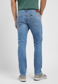 Lyseblå denimjeans med rett passform, med et lærbakpatch og subtile sømdetaljer på lommene. Båret med grå sneakers.