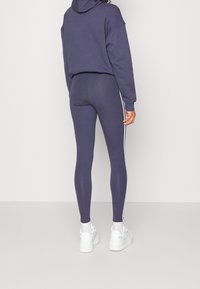 Námořnická mikina a odpovídající legíny s bílými bočními pruhy. Oblečení má volný střih a hladkou strukturu, doplněné o robustní bílé tenisky.