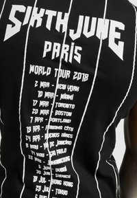 Svart ermeløs skjorte med hvit tekst som viser bynavn og datoer for "Sixth June Paris World Tour 2018," designet i en vertikal layout.
