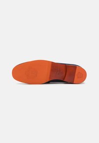 Suela de zapato con una parte inferior de goma naranja lisa y un acento de cuero marrón. Presenta un detalle de logo en relieve y una forma de punta redonda.