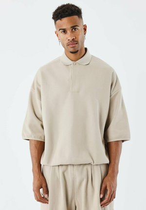 Polo beige avec une coupe décontractée, manches courtes et un bouton au col, associé à un pantalon assorti à coupe décontractée.