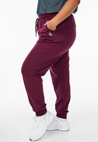Burgunderfarbene Jogginghosen aus weichem Material, mit elastischem Bund, Kordelzug, Seitentaschen und gerippten Bündchen. Mit einem Logoschmuck akzentuiert.