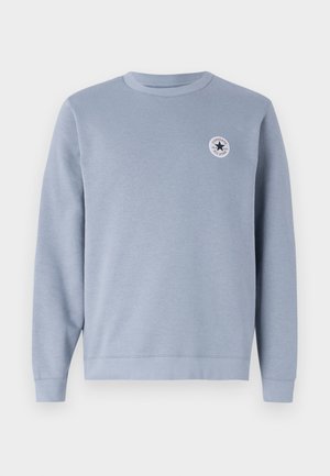 Jasnoniebieska bluza z długim rękawem, okrągłym dekoltem oraz małym, okrągłym logo Converse All Star na lewej stronie klatki piersiowej.