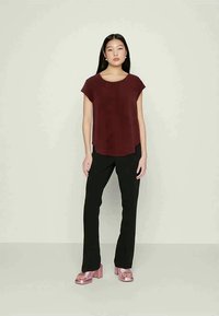 Blusa curta bordeaux com decote redondo, combinada com calças pretas justas e sandálias de plataforma rosa brilhantes. Cores sólidas, design simples.