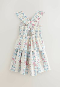 Biele bezrukávové letné šaty s kríženými volánovými ramienkami, viacvrstvovou sukňou a kvetinovým vzorom v modrej, ružovej a oranžovej farbe.