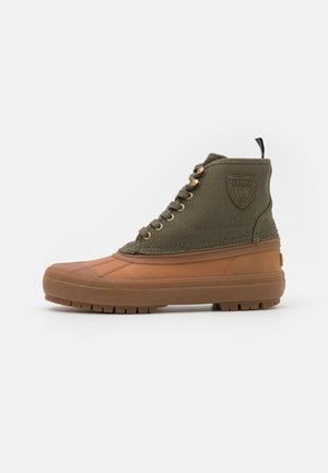 Bottes montantes vert olive avec une semelle extérieure en caoutchouc beige, des œillets dorés et un patch logo sur le côté ; conçu avec une tige en toile texturée.