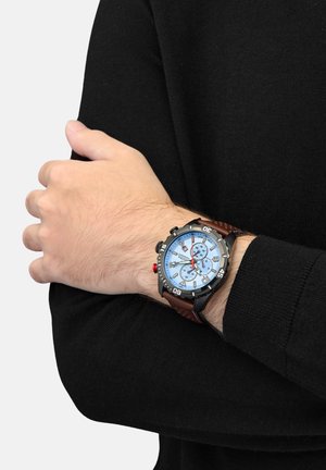 Une montre-bracelet avec un cadran bleu, des accents en argent et un bracelet en cuir marron. Les caractéristiques incluent des cadrans de chronomètre et un bouton-poussoir rouge.