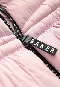 Lyserød quiltet dunjakke med lynlås. Har et sort mærke med teksten "BAKER" fastgjort til lynlåstrækket. Blød, glat tekstur.