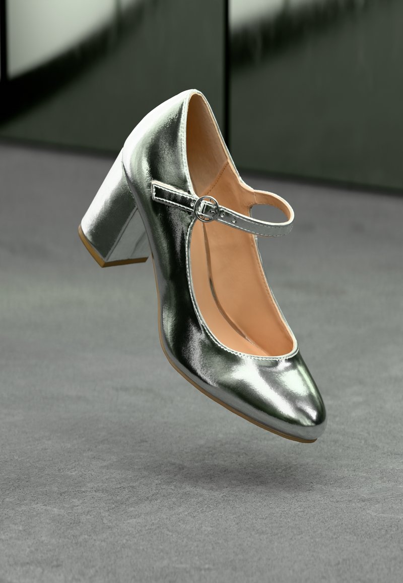 Chaussure Mary Jane à talon haut argentée brillante avec une bride à boucle et un talon bloc sur une surface grise.