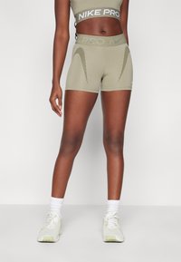 Reggiseno sportivo Nike Pro verde oliva chiaro e pantaloni corti abbinati, con una cintura testurizzata e un motivo a strisce diagonali. Sneakers bianche con inserti in rete.