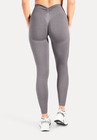 Leggings gris taille haute avec un détail de couture froncée à l'arrière et une texture lisse, assortis à des chaussures de sport blanches.