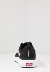 Zwarte sneakers met een bovenwerk van mesh, witte accenten en een gestructureerde zool. Beschikt over een trekband met het label "ULTRARANGE" op de hak. Rode logo op de zool.